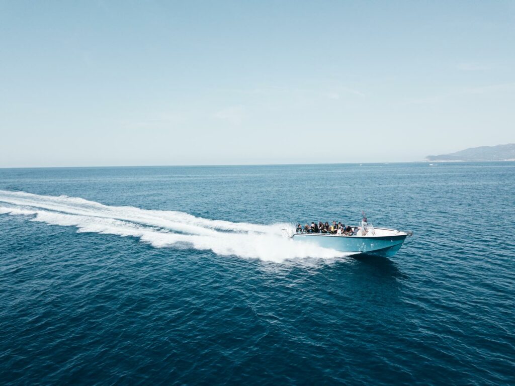 Dive boat speeding across open sea with passengers on board, leaving a white wake, coastline in the distance